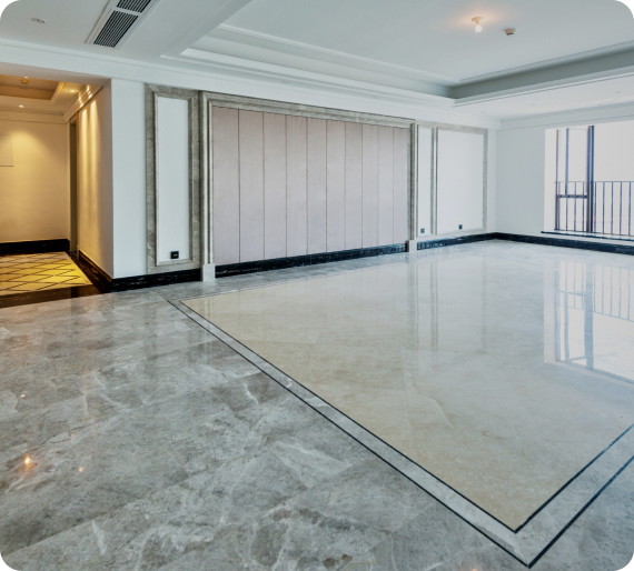 Spacious empty room with marble flooring, recessed lighting, and a large window. Walls are light-colored, and there is a pattern in the floor near the entrance.