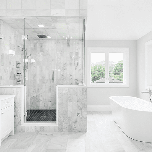 Bright modern bathroom with a glass-enclosed marble shower, a white freestanding bathtub, and large windows.